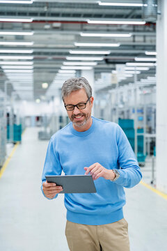 Engineer using tablet in modern production hall with machinery
