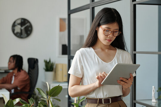 Woman using a tablet in a modern office setting with a colleague in the background