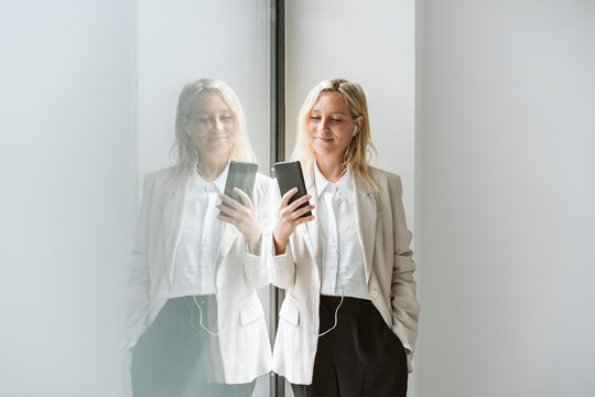 Businesswoman looking at mobile phone at glass wall