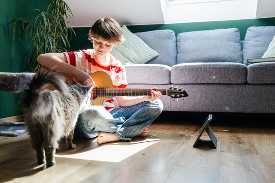 Girl playing guitar on floor with cat and digital tablet