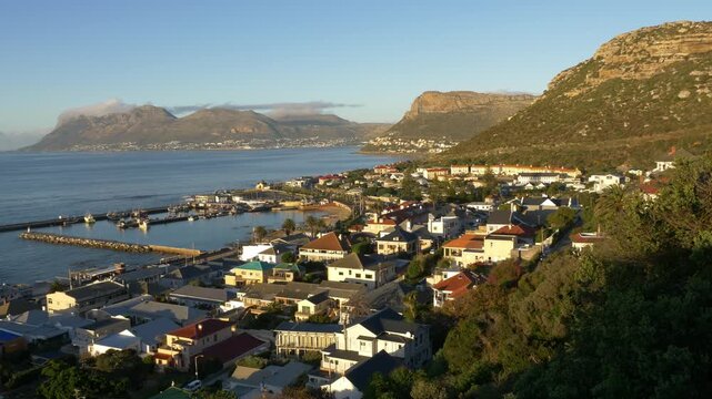 4k 30fps aerial view over Kalk Bay Harbour and the colourful seaside village, looking across the calm waters of False Bay towards Simon's Town on the Cape Peninsula, Western Cape, South Africa.