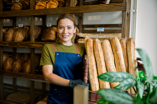 Happy saleswoman holding basket of fresh bread in bakery