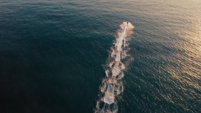 Aerial view of a jet ski speeds across the water, leaving a distinct trail behind as it cuts through the sunlit ocean