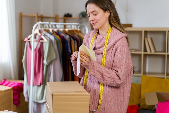 Clothing designer packs cardboard box with order in home studio