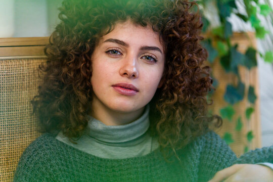 Calm woman with curly hair looking at camera indoors