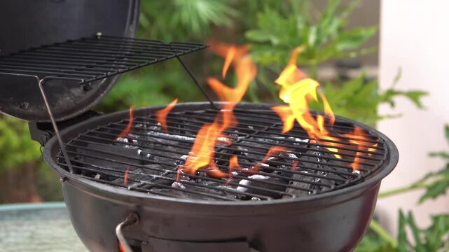 Close-up shot of a BBQ grill being prepared with open flames, charcoal heat, and outdoor greenery. Ideal for food, summer cookout, and lifestyle projects.