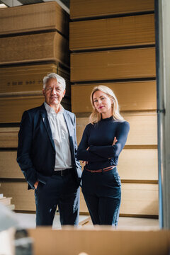 Smiling senior businessman with colleague standing in front of stacked wood