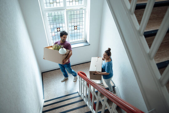 Happy man and woman with cardboard boxes moving up on staircase
