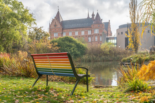 Sweden, Skane County, Malmo, Rainbow colored bench standing in front of park pond with Malmo City Library in background