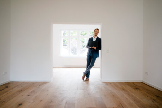 Estate agent waiting in newly refurbished home, holding laptop