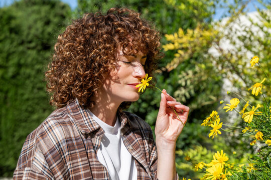 Woman smelling a yellow flower in a sunny spring garden