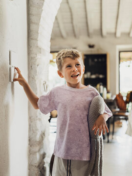 Smiling boy touching light switch at home with stuffed toy