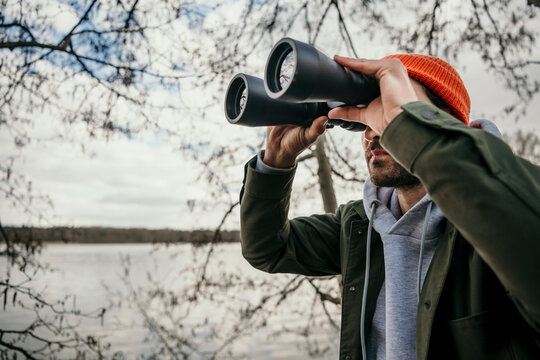 Man looking through binoculars by bare tree
