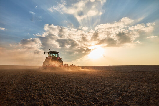 Tractor plowing and cultivating field at sunset