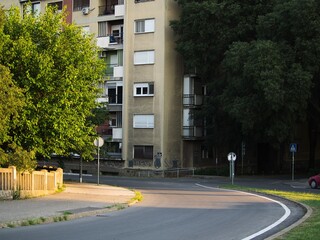 Obraz premium An empty curved asphalt road in a residential neighborhood city street at golden hour sunset with an apartment building and green trees.