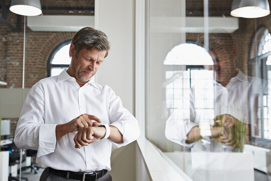 Smiling businessman in office looking at smartwatch