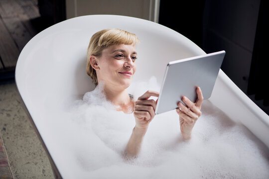 Portrait of relaxed woman taking bubble bath while using tablet