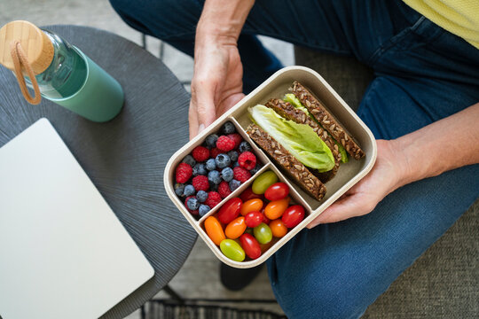 Hands of man holding lunch box with healthy food on sofa