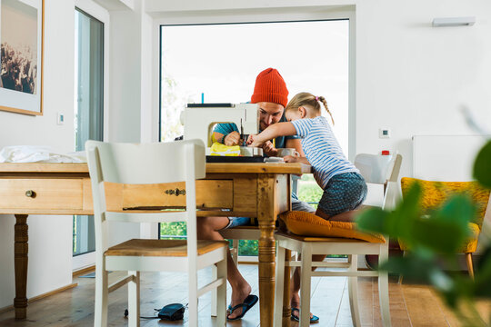 Father and daughter at home using sewing machine