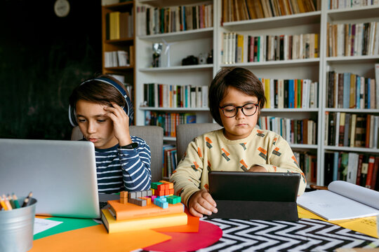 Boy e-learning through laptop while male friend studying with digital tablet at table