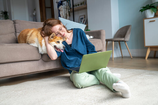 Woman using laptop and hugging pet dog in living room
