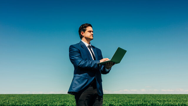 Businessman using laptop in green wheat field under blue sky