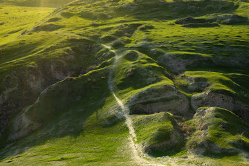 Naklejka premium Green grass-covered hills of Afrasiyab archaeological site in Samarkand with a winding footpath through eroded gullies. Ideal for travel, history, and heritage publications.