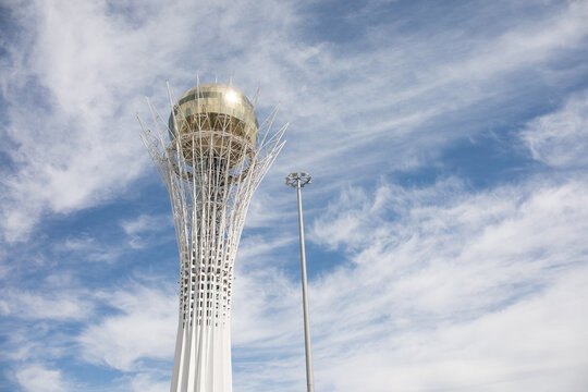 Golden sphere atop tall, white, slender tower. Twisting metal arms surround the orb. Sky is blue with scattered, wispy clouds. Astana, Kazakhstan - June 24, 2026