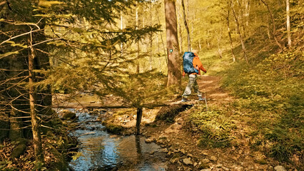 Fototapeta premium A hiker navigates a forest trail beside a flowing stream, surrounded by autumn foliage. Showing the serene beauty of nature, emphasizing purity and the outdoor experience.
