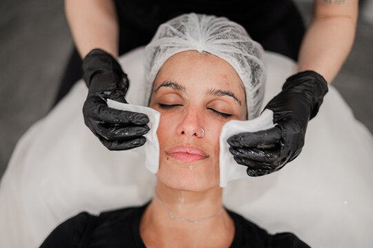 Beauty therapist wiping facial cream off clients face using sterile gauze pads