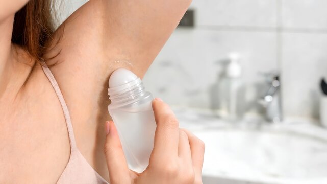Woman standing in a bright bathroom applying antiperspirant deodorant to her underarm, representing daily personal grooming, hygiene routine, and summer self-care concepts for beauty stock photos