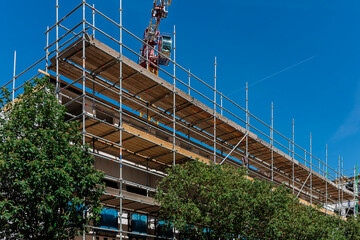 Fototapeta premium Scaffolding covers a building under construction with a tower crane behind, set against a blue sky.