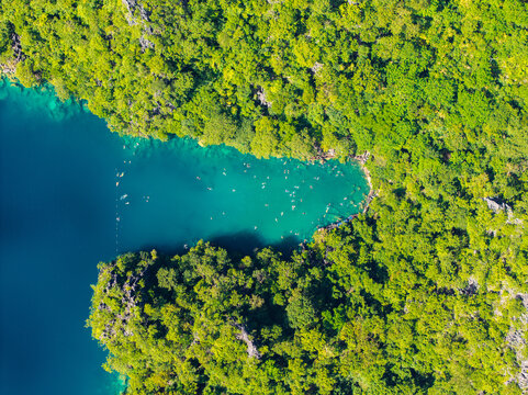 Aerial view of Kayangan Lake with turquoise water surrounded by lush tropical forest and limestone cliffs, with people swimming in the lake in Coron, Mimaropa, Philippines.