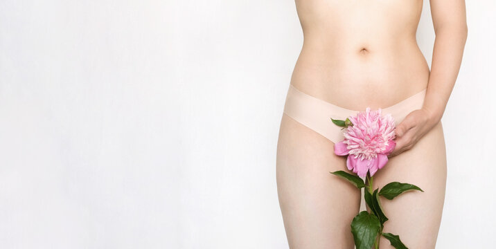 A woman holds a pink peony flower near her hips. Concept of femininity. Horizontal banner with a place for text