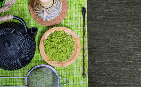 Matcha green tea powder on wooden plate with bamboo whisk and cast iron teapot. Traditional japanese tea ceremony preparation accessories. Healthy organic beverage concept overhead view
