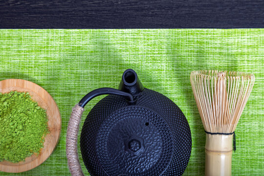 Matcha tea powder with iron teapot and bamboo whisk. Japanese tea ceremony equipment on green mat. Healthy organic green tea preparation for mindfulness, meditation and wellness lifestyle