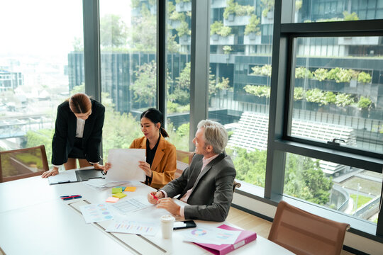 Corporate professionals examine business reports during office discussion. Executive leadership, teamwork, project management, financial review, workplace collaboration.