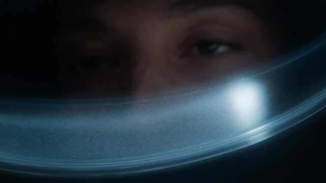 Close up of astronaut eyes looking through helmet visor in dark space environment.