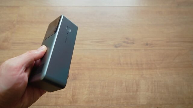 Single hand holding power bank portable charger close up modern external battery device with copy space on right. Minimal tech composition over wooden background clean mobile charging accessory