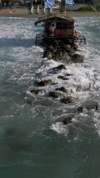 Vertical aerial, panoramic view of the northern coast of the island of Crete. Waves crashing against the rocky pier near the town of Agia Marina and Platanias, Crete, Greece