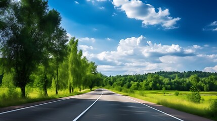 Fototapeta premium Straight road lined with tall green trees and lush forest, extending into distance under bright blue sky with clouds.