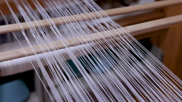 Close-up tracking shot following warp threads through the wooden frame of a traditional loom. Textile craftsmanship used in the creation of handmade Albanian rugs, bags, flags, and decorative fabrics.