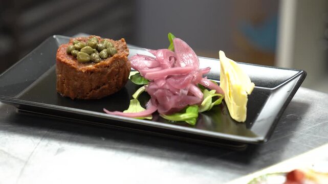 Professional chef preparing a delicious raw beef tartare with capers and pickled red onion