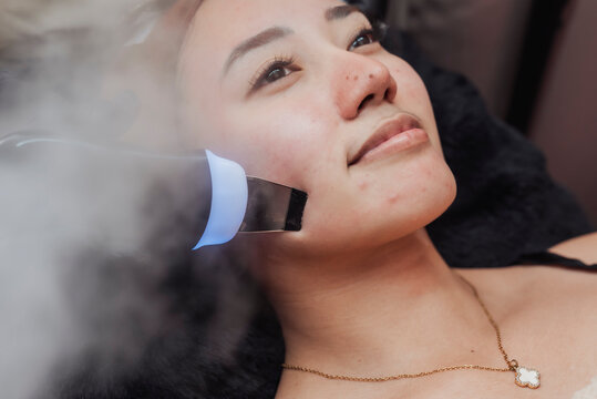 Ultrasonic skin scrubber facial with steamer on Southeast Asian woman for deep pore cleansing, gentle exfoliation and smoother healthier skin