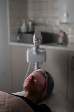 Woman lies on treatment bed with a mask covering her eyes, undergoing a skincare procedure