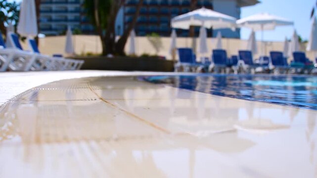 Low-angle view of sunny hotel pool edge with sun loungers and umbrellas. Luxury resort, vacation, and summer travel concept