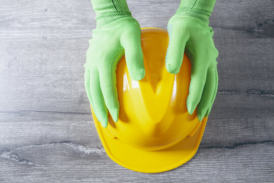 Hands in green protective gloves holding yellow hard hat