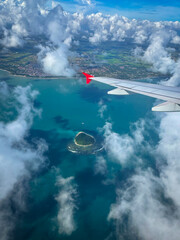 Naklejka premium AERIAL: Tip of an airplane wing above turquoise coastal water, drifting clouds and a small island. Traveling by plane over tropical coastline of island of Sumatra, Indonesia, with vivid sea colors.