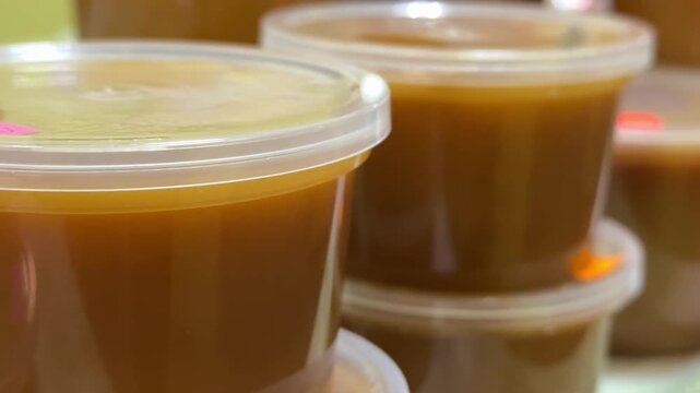 Close-up honey jars on counter warm amber honey in clear plastic containers stacked on cloth market display glossy texture visible