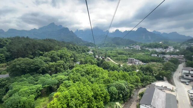 Aerial view of cable car riding over green mountain landscape time lapse. Gondola lift transport system in valley near village. Travel excursion nature, scenic mountain sightseeing location timelapse.